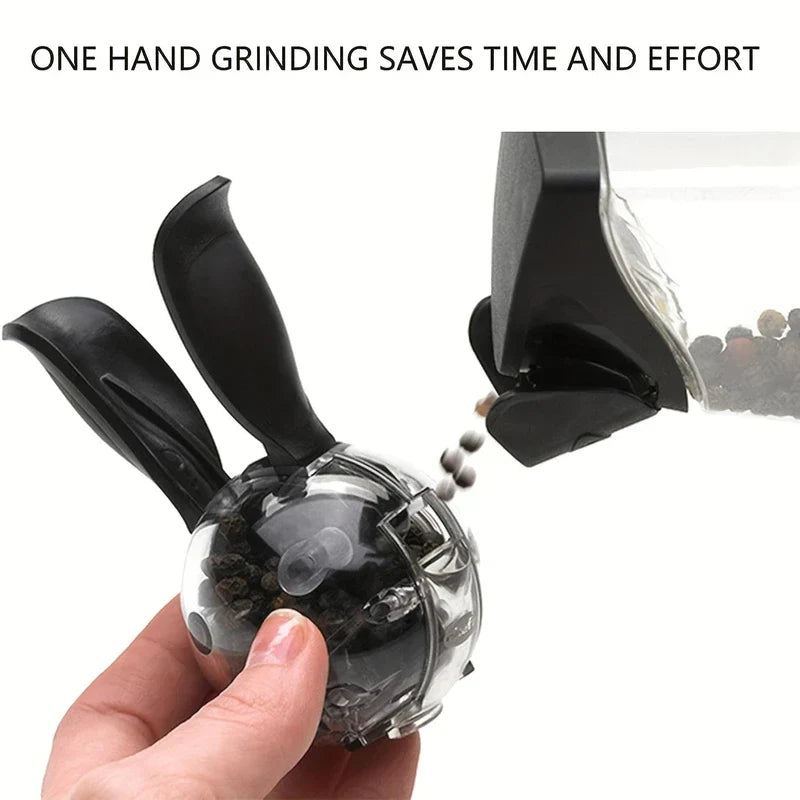 Pepper Grinder - Hand holding a clear two-handled manual spice grinder as peppercorns are added into its open top