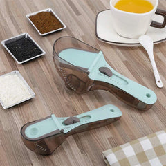 Kitchen Tool - Two adjustable measuring scoops rest on a wooden table beside ingredient trays, a cup of orange liquid, and a white spoon.