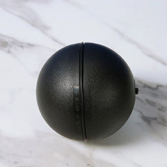 Microfiber Robotic Mop Ball Cleaner - Black spherical plastic object with a central seam, raised side tab, and small nub on its right edge, resting on marble.
