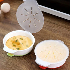Microwave Egg Cooker - Two open and closed cooking bowls on wood counter, one holding cooked steamed egg garnished with chives next to whole eggs