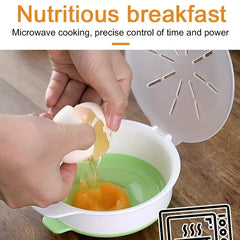 Green and white microwave egg cooker with lid open, hands cracking an egg into it on a wood-grain surface.