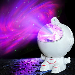Mini Astronaut Projector - White astronaut-shaped light projecting swirling purple and pink nebula with scattered green stars, placed on a cratered moon-like surface