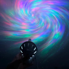 Mini Astronaut Projector - Hand holding a small black projector casting a swirling rainbow spiral with small white dots onto a dark surface