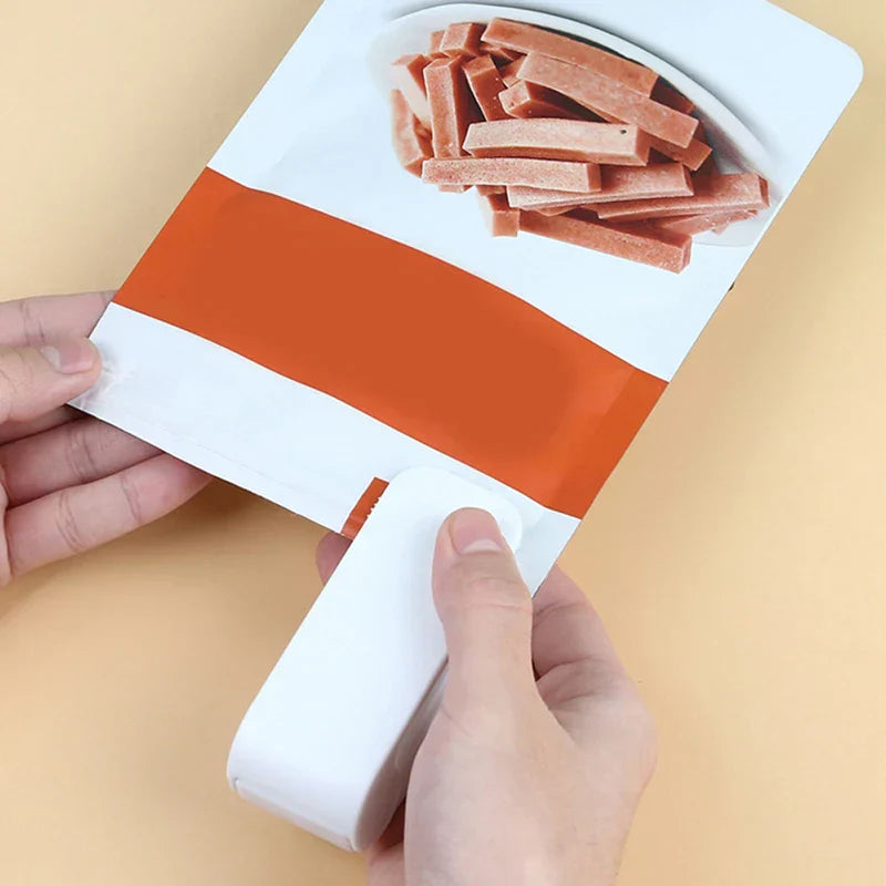 Heat Sealer - White mini sealer being used to seal a snack bag held by two hands on a pale yellow surface