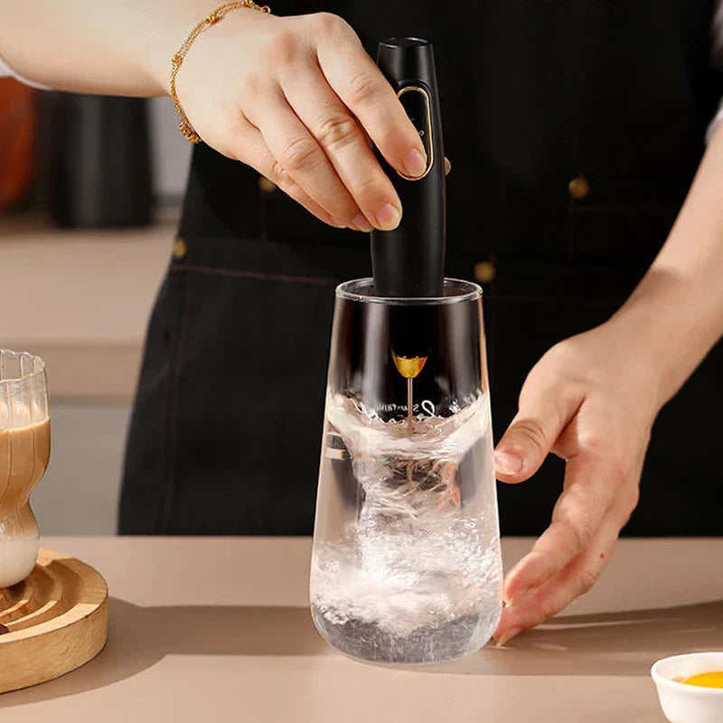 Electric Milk Frother - Black handheld electric frother being operated by a person inside a clear glass of liquid