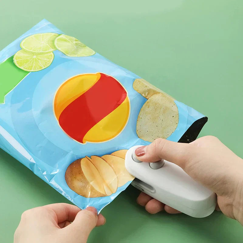 A hand holding a white handheld plastic device against the edge of a blue potato chip bag, with another hand holding the bag.