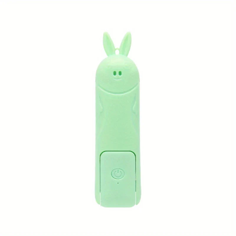 ventilador mini - dispositivo electrónico con forma de conejo de dibujos animados en verde menta claro con botón de encendido, cara sonriente y orejas erguidas sobre fondo blanco liso