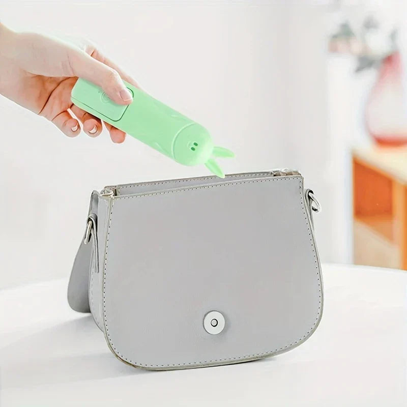 Mini Fan - Hand holding a green bunny-themed folding fan above an open gray saddle bag on a white surface