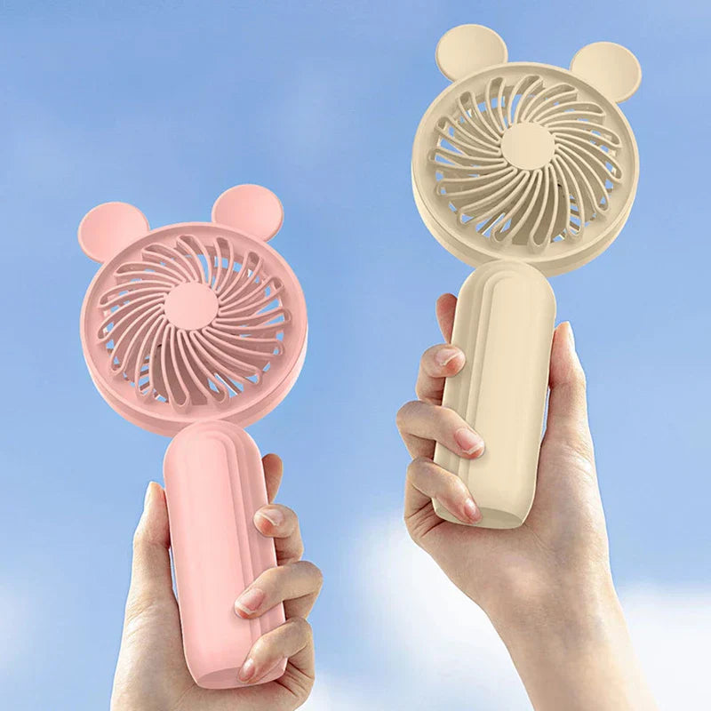 Mini Manual Handheld Squeeze Fan - Two colored bear-ear design fans held in separate hands against bright blue sky