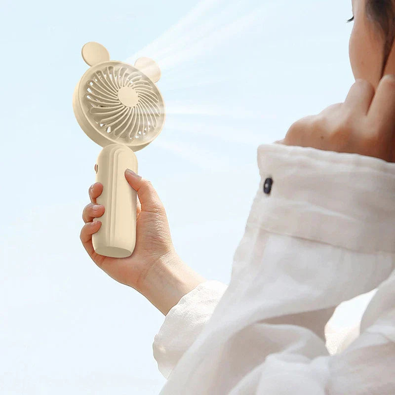 Mini Manual Handheld Squeeze Fan - Cream colored bear-ear design fan held up to provide cooling for a person outdoors