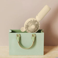 Mini Manual Handheld Squeeze Fan - Mint green tote bag in foreground, with an off-white handheld fan resting partially inside it against a neutral background