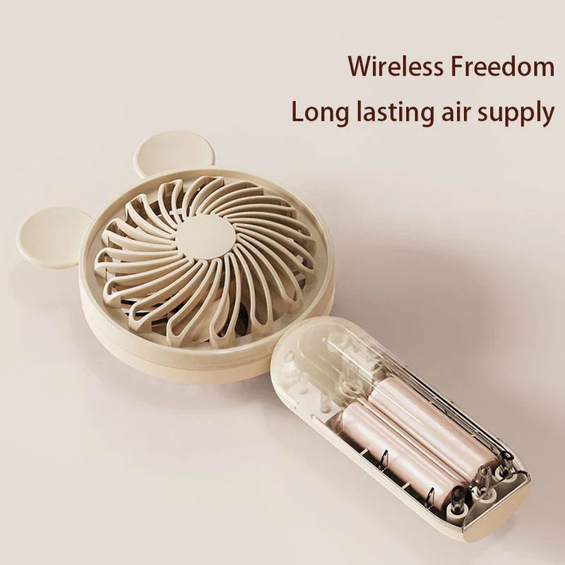 Mini Manual Handheld Squeeze Fan - Off-white handheld fan with its handle opened showing two batteries inside, text reading Wireless Freedom Long lasting air supply to the upper right