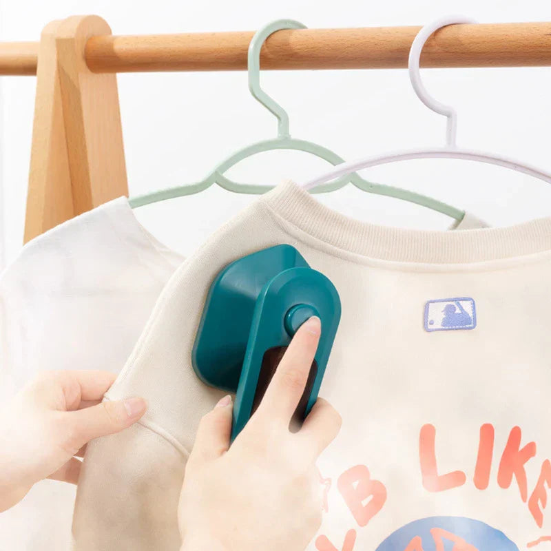 Electric Travel Iron - Person pressing a teal handheld iron onto the shoulder of a hanging light-colored sweatshirt