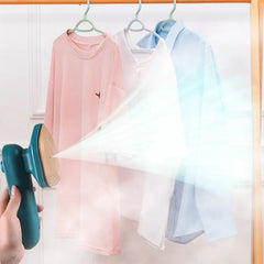 Electric Travel Iron - Hand holding a teal portable handheld garment steamer emitting steam toward three hanging shirts on hangers