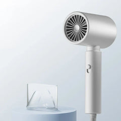 White handheld hair dryer standing upright, with its clear concentrator nozzle placed on a light blue pedestal beside it.