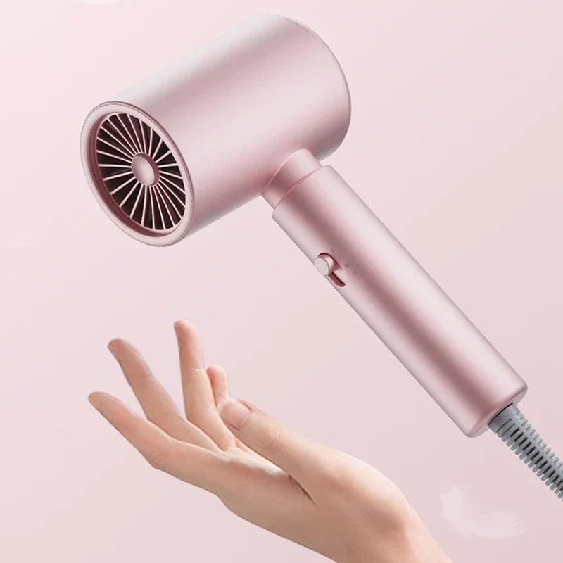 Hair Dryer - Matte pink hairdryer tilted, held above an open palm to show its lightweight handheld form