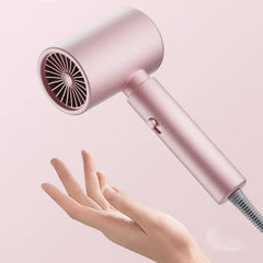 Hair Dryer - Matte pink hairdryer tilted, held above an open palm to show its lightweight handheld form