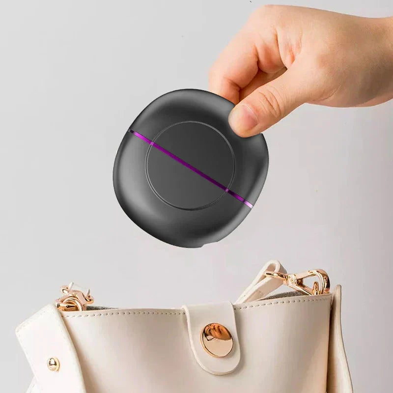 Portable Hair Straightener Brush - Hand holding a small rounded dark gray device with purple accent line, positioning above an open white bag