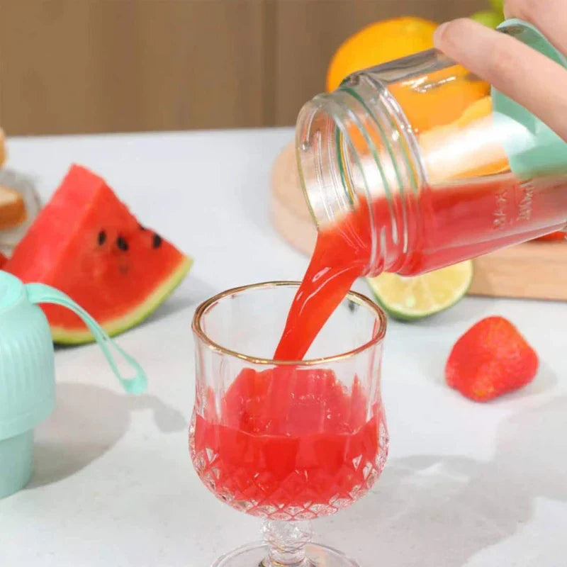 Mini Juicer Blender - Hand pouring red juice from a mint green blender into a small glass, with fruit and a blender lid nearby
