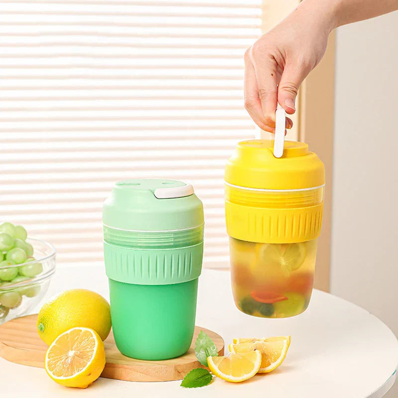 Portable Juicer Blender - Two blenders in yellow and mint green displayed on a tabletop alongside fresh lemons and green grapes, with a hand lifting the yellow unit by its carry loop