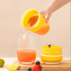 Portable Juicer Blender - Hand pouring orange-pink juice from a yellow cup into a glass, with a blade component and fruit nearby