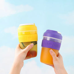 Portable Juicer Blender - Two hands holding yellow and purple portable cups, against a light blue sky background