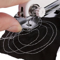 Close-up of a handheld sewing machine stitching white concentric patterns on black fabric, with fingers guiding the fabric