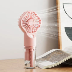 Usb Fan - Pink handheld misting fan sitting on a wooden desk next to an open magazine, demonstrating active airflow