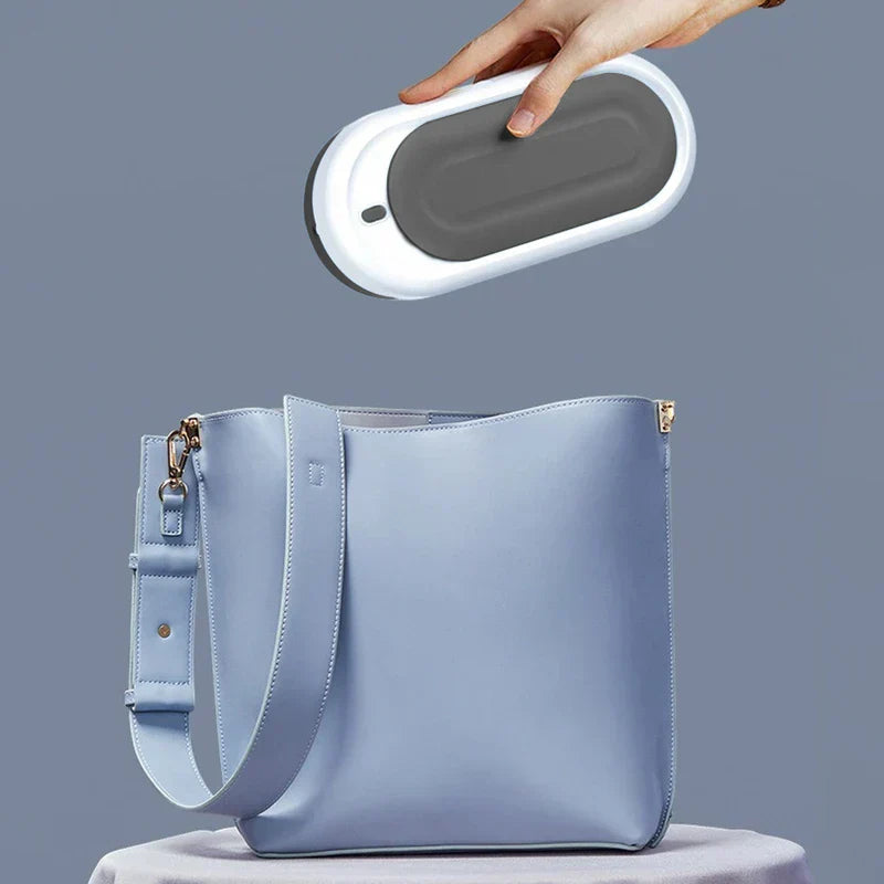 Ultrasonic Jewelry Cleaner - Hand placing a white and gray compact cleaner into a light blue shoulder bag