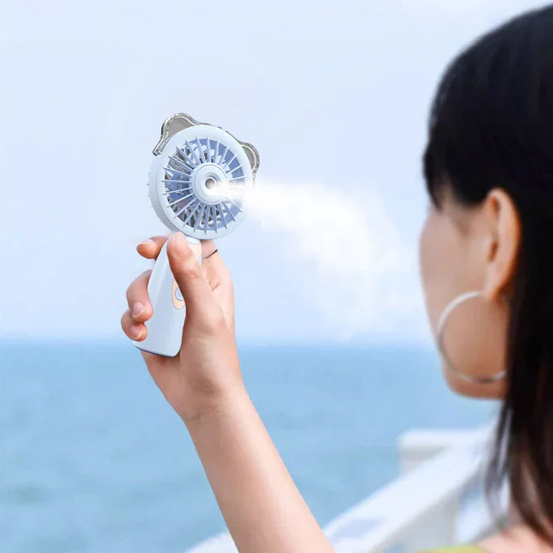 Humidifier - Person holding the handheld fan, which emits a mist spray toward their face, with sea in background