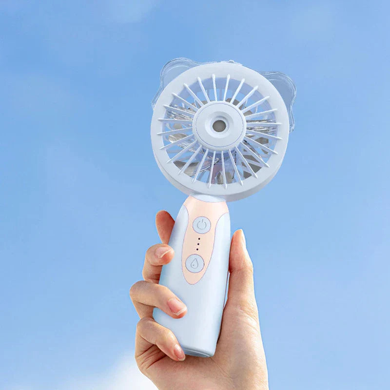 Humidifier - Hand holding a light blue handheld spray fan with cat ear accents against a clear blue sky
