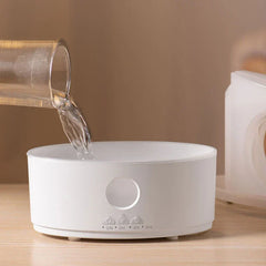 Cool Mist Humidifier Diffuser - Water being poured into the open base of the white diffuser unit on a wood surface.