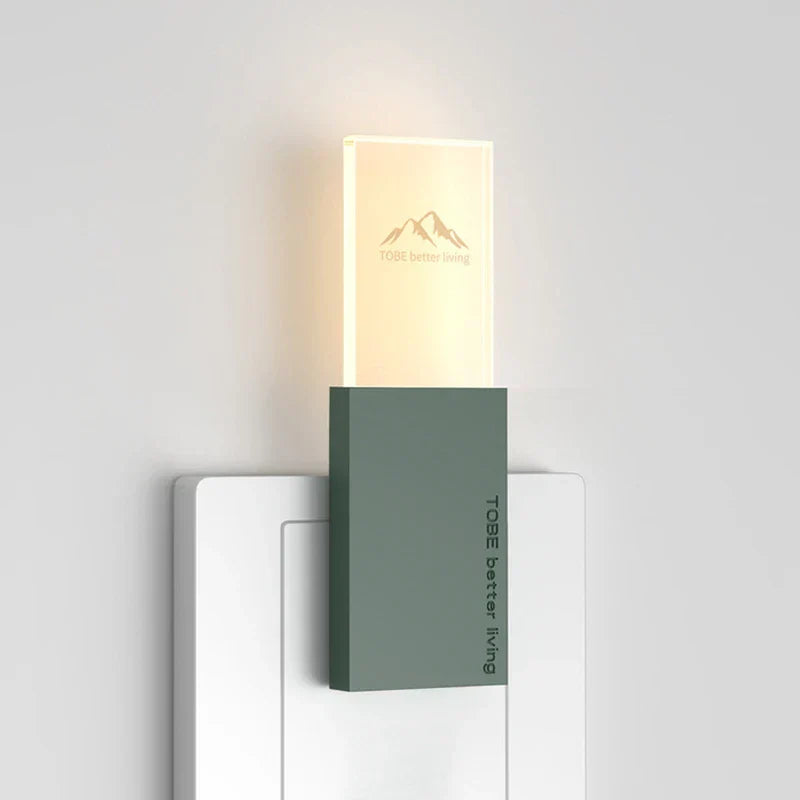 Mosquito Repellent Night Light - Dark green rectangular USB plug-in night light, lit with warm glow, inserted in a white wall socket, viewed against a plain light wall