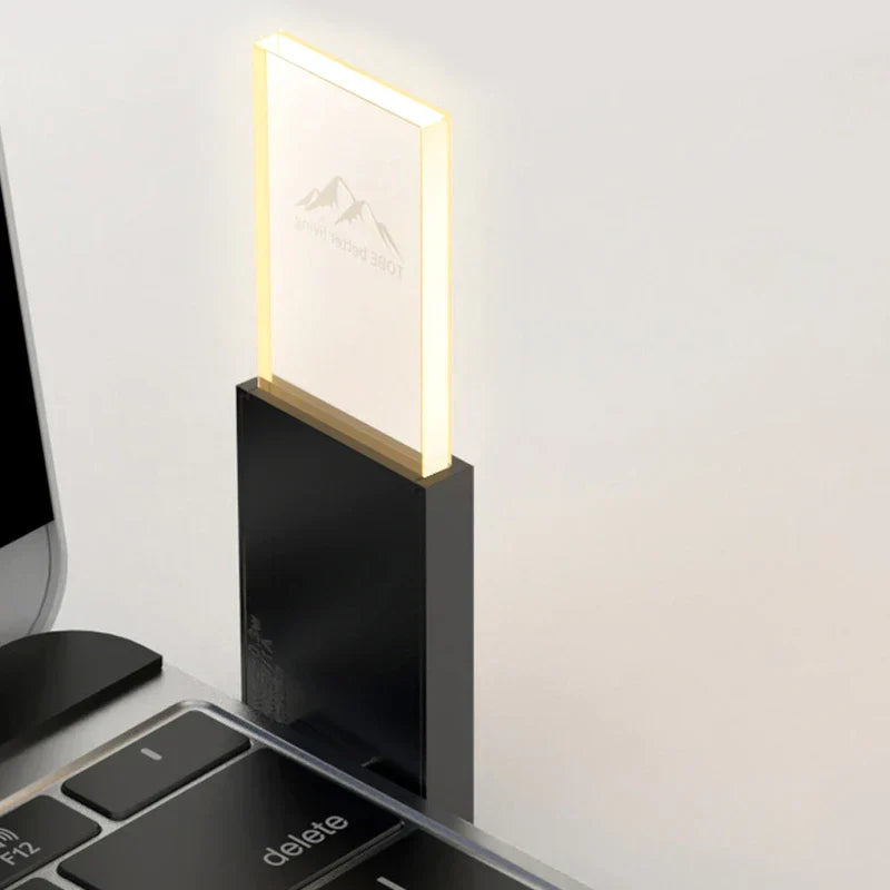 Mosquito Repellent Night Light - Small lit light plugged into a laptop keyboard slot, glowing pale yellow panel showing faint mountain logo