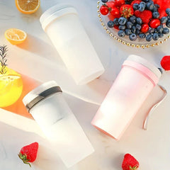 Three portable juicer blenders in white, black accented, and pink lie on a marble surface, surrounded by fresh berries, lemon slices, and a yellow drink.