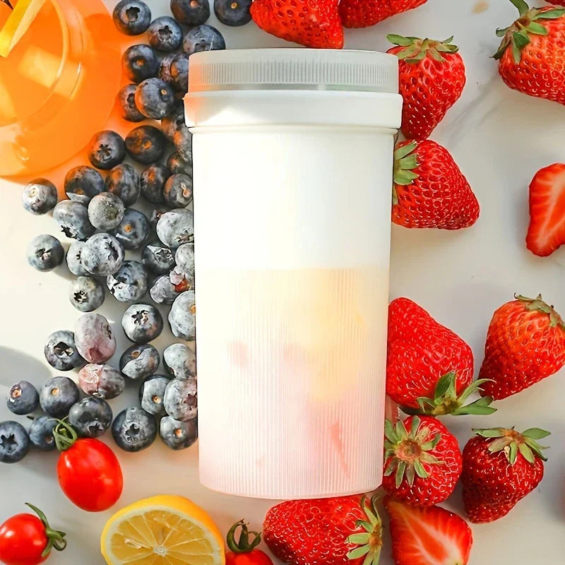 White juicer blender sits surrounded by fresh strawberries, blueberries, lemon, and cherry tomatoes on a marble surface.