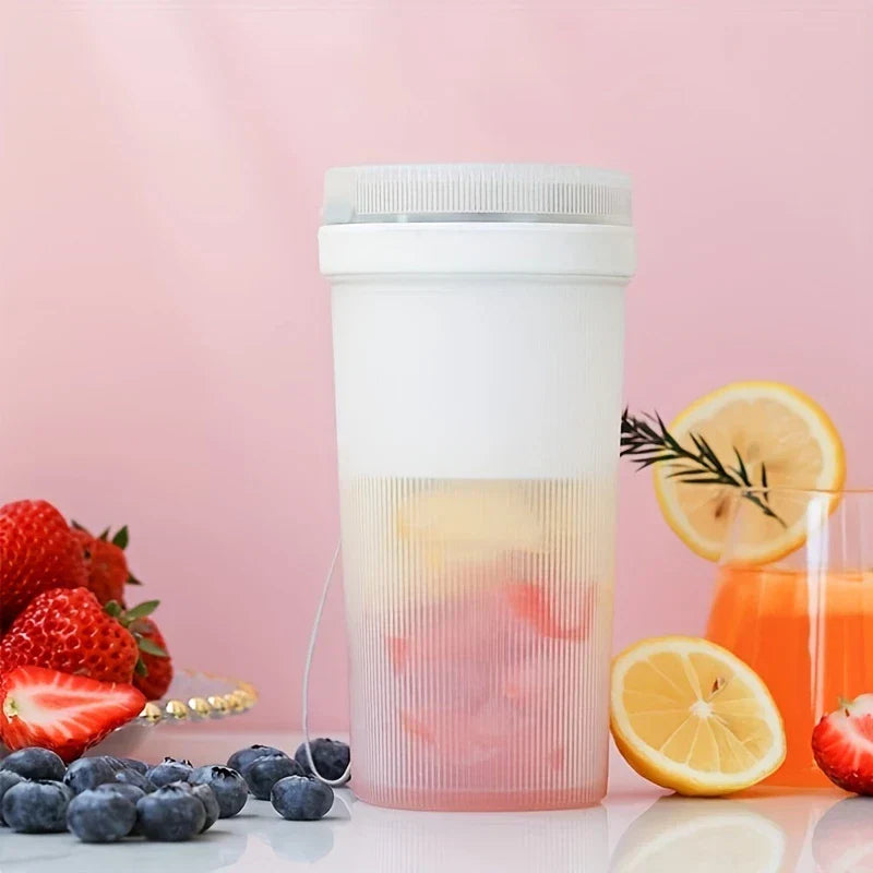 White juicer blender with visible fruit inside rests near strawberries, blueberries, lemon slices, and an orange drink glass.