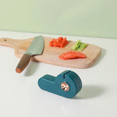 Manual Knife Sharpener - A teal sharpener sits on a white countertop in front of a wooden cutting board holding sliced vegetables and a knife