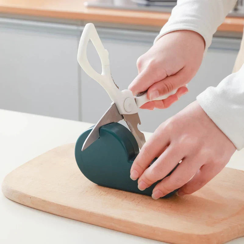 Manual Knife Sharpener - A person holding kitchen scissors places the blade into a teal sharpener resting on a wooden cutting board