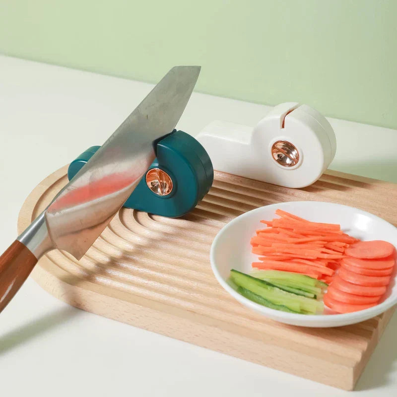 Manual Knife Sharpener - A kitchen knife rests in a teal sharpener, with a second white sharpener, grooved wooden cutting board, and plate of cut vegetables nearby.