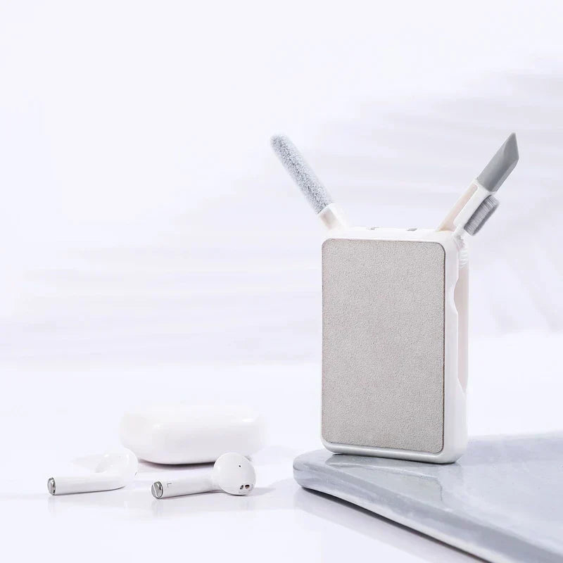 A cleaning brush set sits beside white wireless earbuds and their charging case on a light surface.