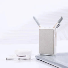 A cleaning brush set sits beside white wireless earbuds and their charging case on a light surface.