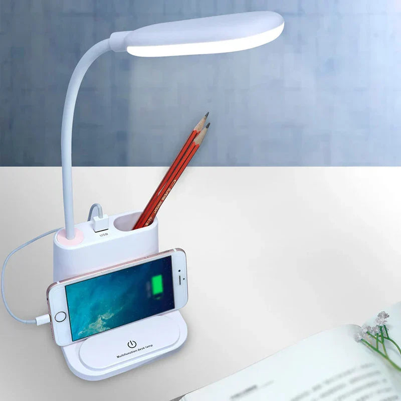 Led Desk Lamp - White desk lamp with pencils stored in its organizer, a smartphone resting on the base stand connected to the built-in USB port, lit to cast task light