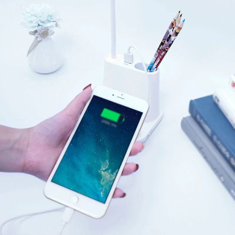 Led Desk Lamp - White pen holder desk lamp showing a USB port charging a connected smartphone, with colored pencils stored in the pen holder.