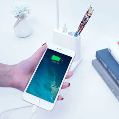Led Desk Lamp - White pen holder desk lamp showing a USB port charging a connected smartphone, with colored pencils stored in the pen holder.