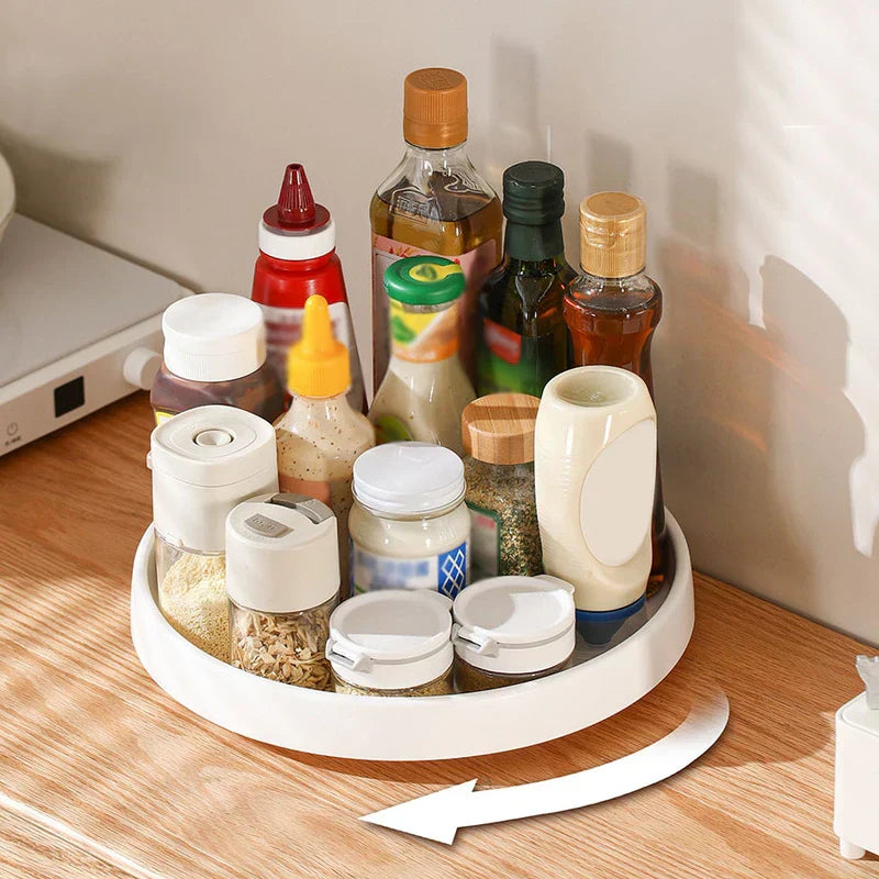Rotating Storage Turntable Tray Organizer - Round tray holding assorted cooking oils, spices, and condiments on a wood kitchen counter with rotation indicator arrow