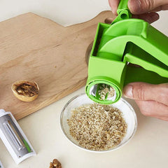Vegetable Grater - Hand operating the rotary tool to dispense chopped walnuts into a small glass bowl, with a wooden cutting board and vegetable peeler nearby