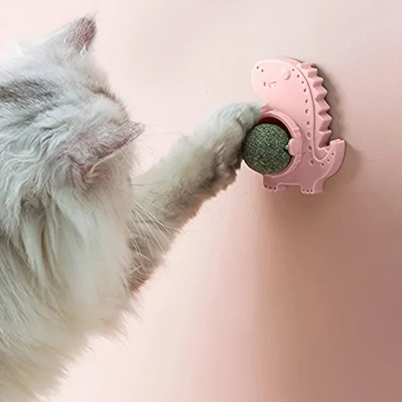 Natural Catnip Ball Wall Lollipop Toy - Fluffy longhair cat extending a paw to touch a green ball in a pink dinosaur-shaped wall-mounted toy