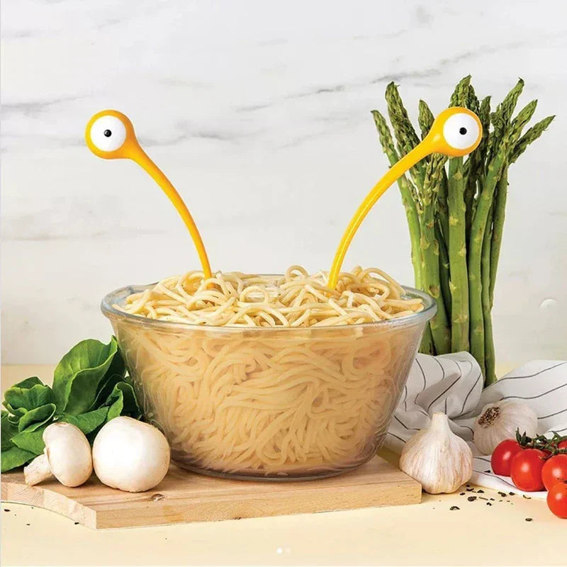 Soup Ladle - Yellow serving utensils placed in a glass bowl of noodles, styled with fresh produce on a wooden cutting board