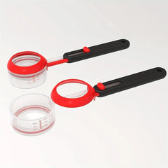 Cucharas medidoras: dos cucharas medidoras ajustables, una ensamblada con una taza transparente acoplada, una taza transparente separada, sobre un fondo liso blanco apagado.